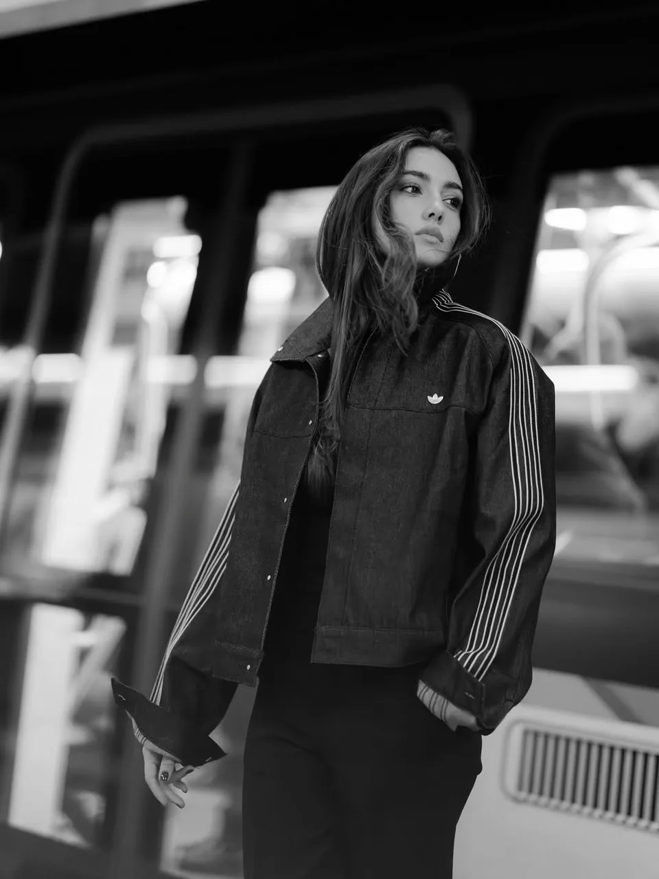 Zeudi in a long dark coat on a station platform, photographed in black and white.