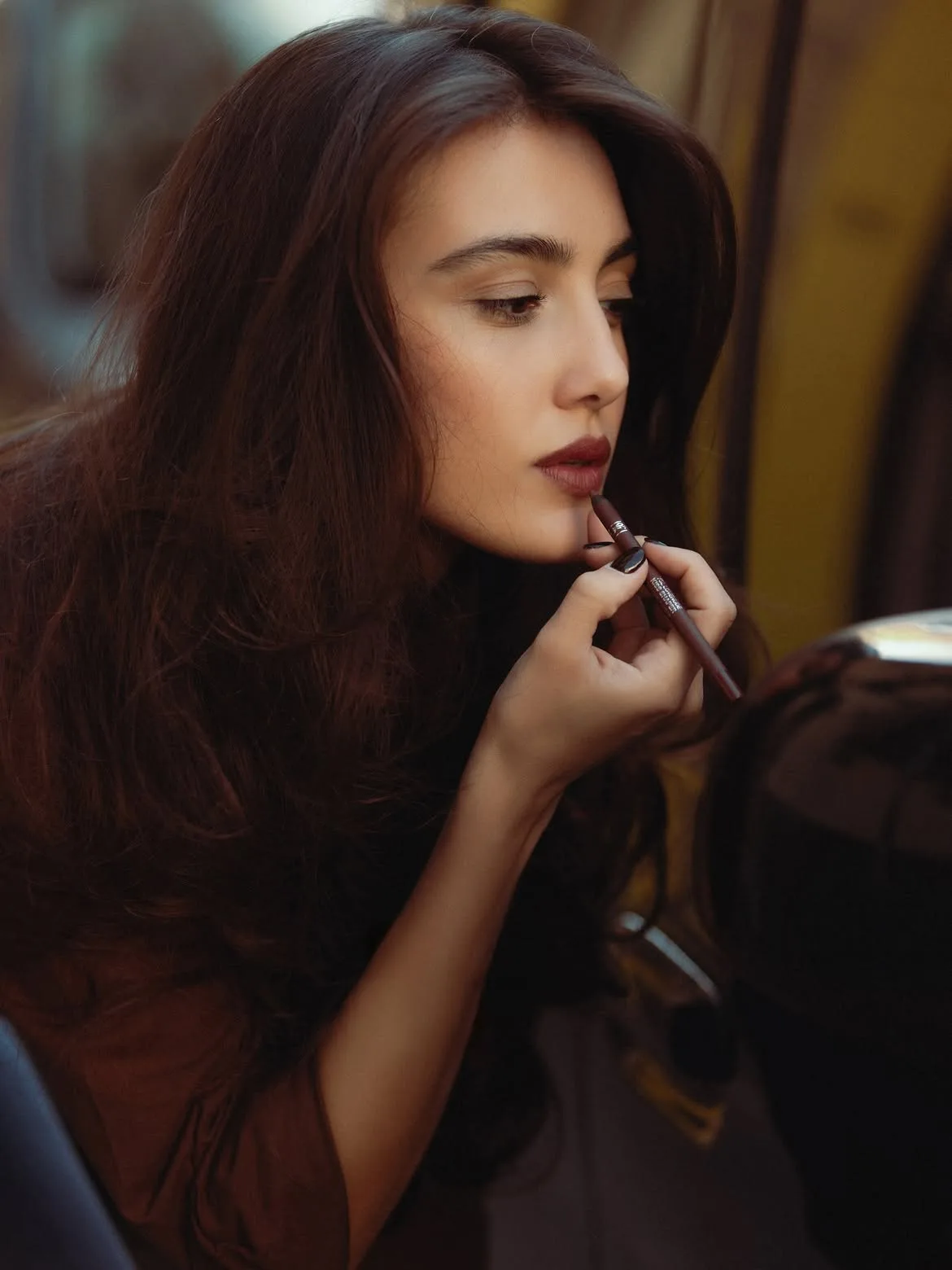 Zeudi applying lipstick while looking into a compact mirror.
