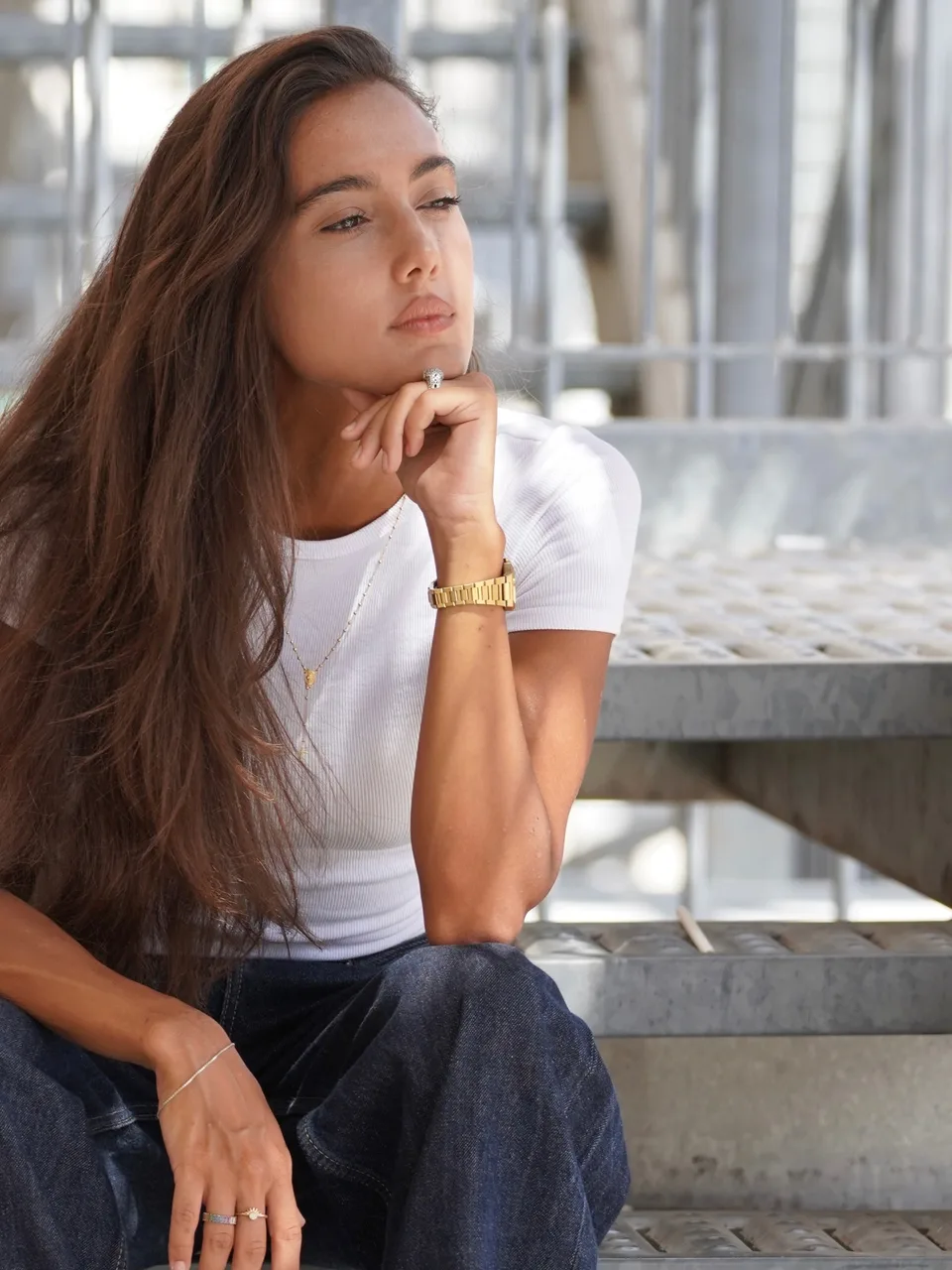 Zeudi in a white T-shirt and jeans, seated beside a bright window.