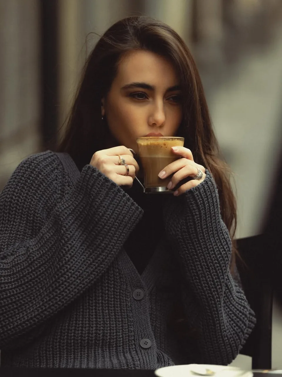 Zeudi enjoying a cup of coffee while looking aside in a dark knitted sweater.