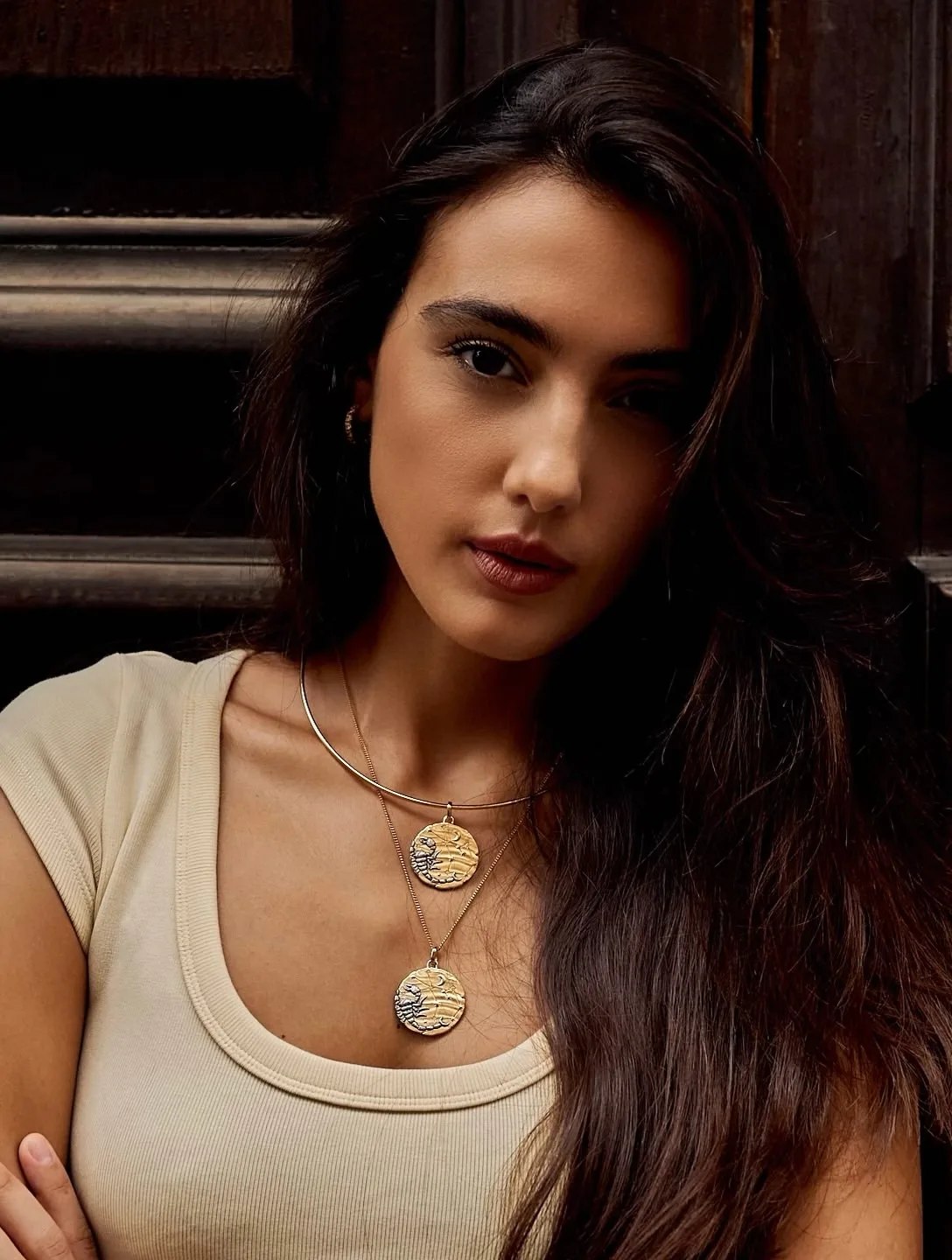 A close portrait of Zeudi in a cream top with layered gold necklaces.